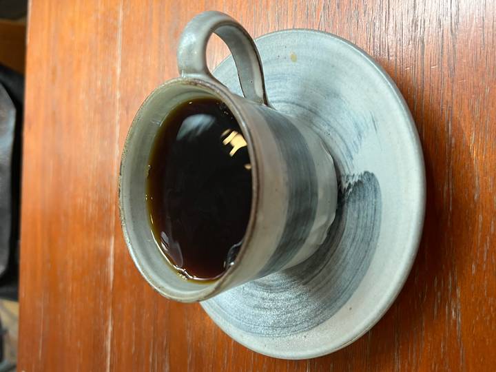 Close-up of a ceramic cup filled with black coffee on a matching saucer placed on a wooden table surface.