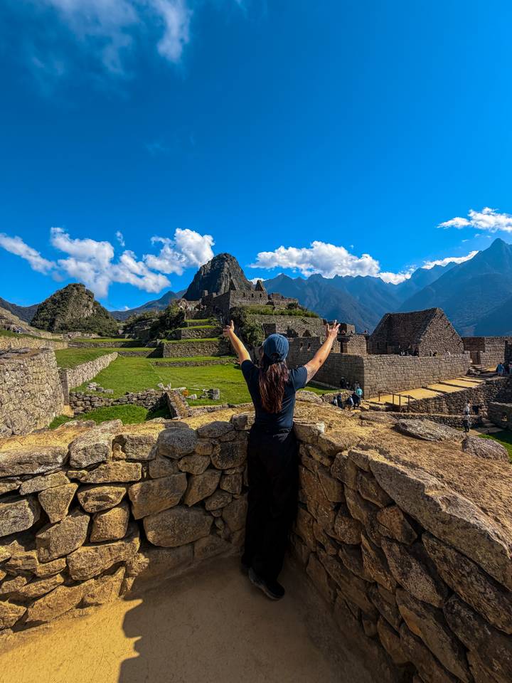 Traveler raises arms in triumph overlooking the stone terraces and peaks of Machu Picchu.