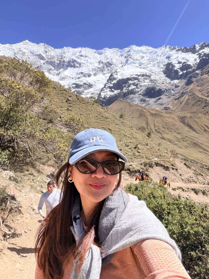 Selfie on a rugged mountain path with snow and horses in the distance.