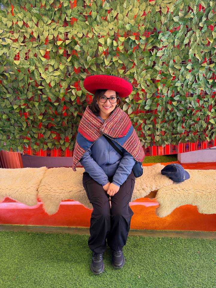 Visitor dressed in traditional Peruvian clothing sitting indoors against a colorful textile backdrop.