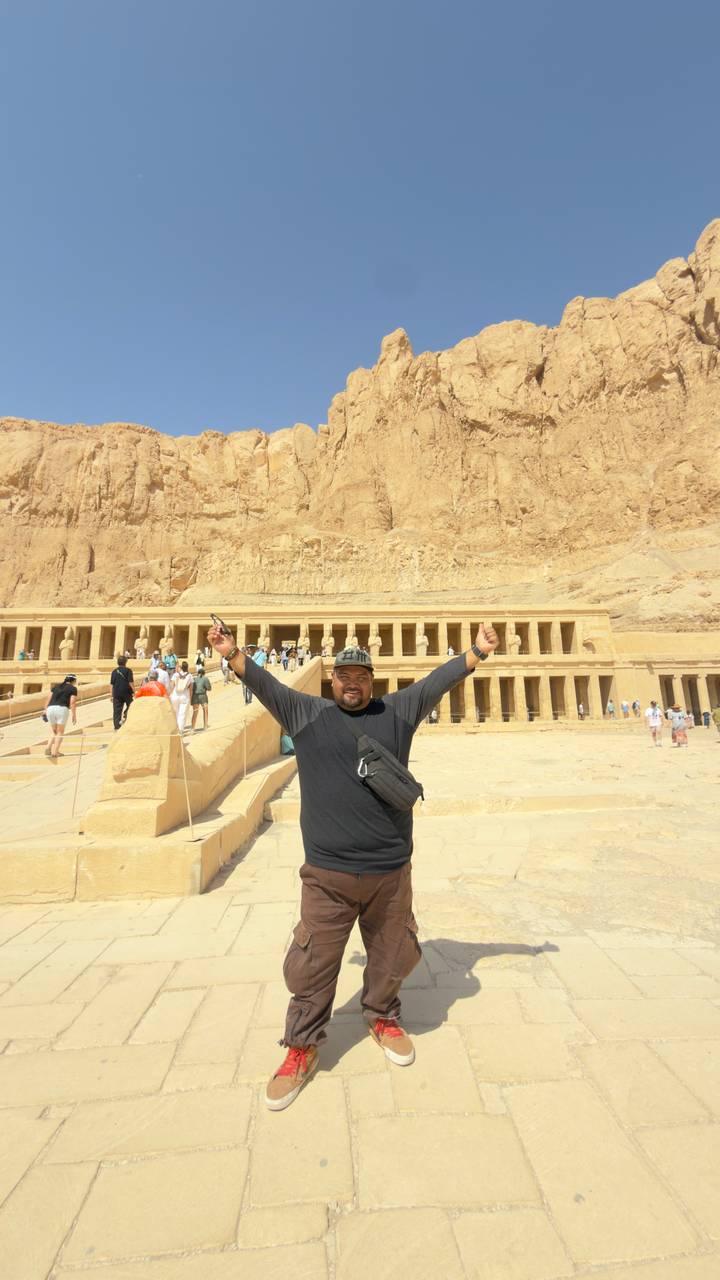 Traveler celebrates in front of the Temple of Hatshepsut with arms raised.