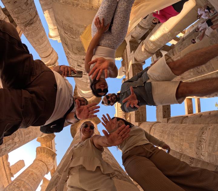 Creative low-angle shot of friends reaching toward the camera amid massive hieroglyphic columns.