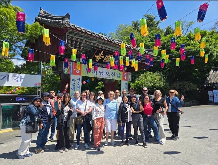 Tour group poses beneath a traditional Korean temple gate decorated with colorful hanging lanterns.