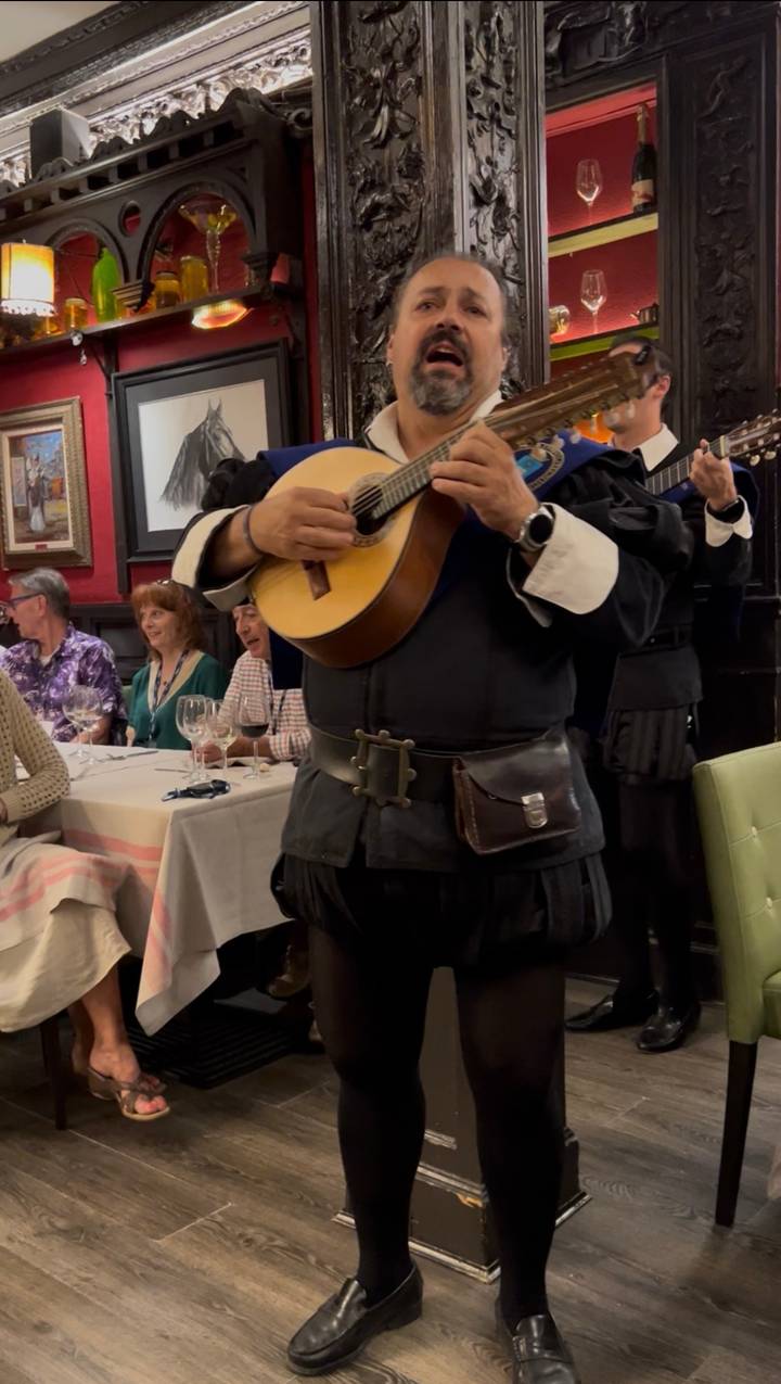 Musician in traditional attire plays classical guitar among dining guests in a Spanish restaurant.