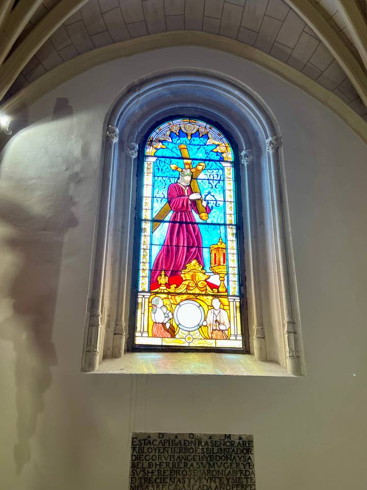 Vibrant stained-glass window featuring a robed figure inside a dimly lit church interior.