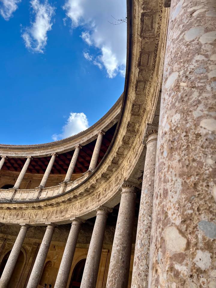 Stone colonnade and curved arcade of a Renaissance palace set against a blue sky.