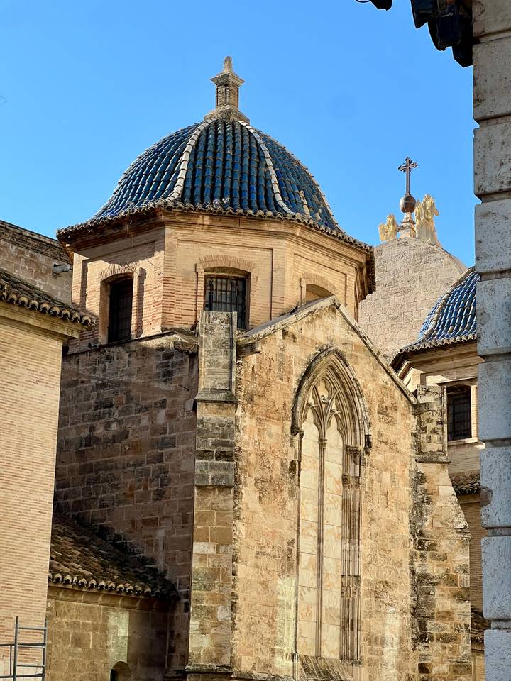 Historic brick and stone chapel with tiled domes and Gothic window details lit by late–day sunlight.