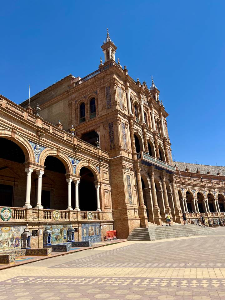 Tower and arched galleries of Plaza de España in warm sunlight against a clear blue sky.