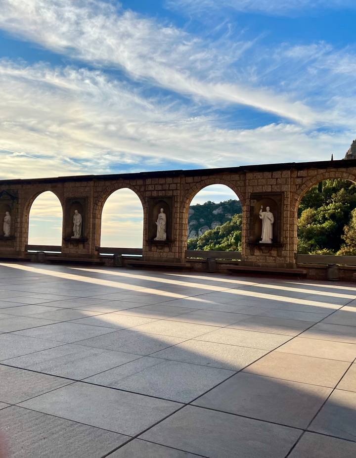 Stone arcade with statues overlooking mountains and sky at Montserrat monastery.