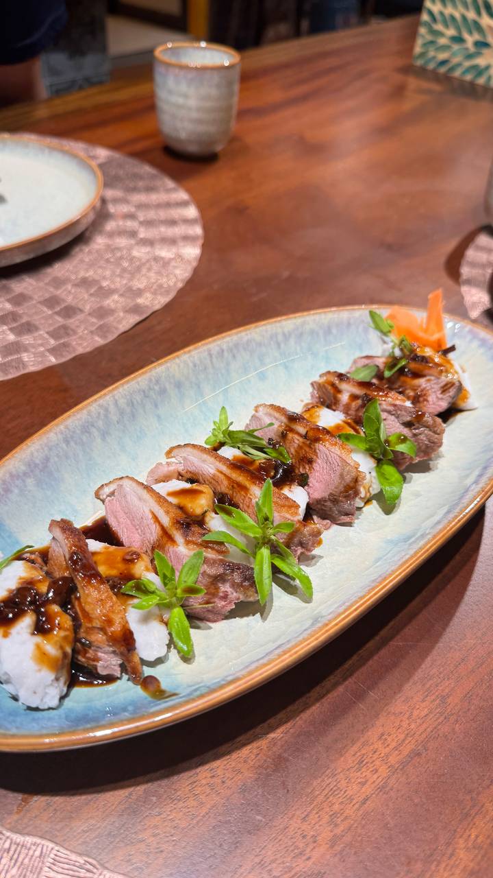 Plated slices of glazed duck breast garnished with herbs arranged neatly on a ceramic dish in a restaurant.