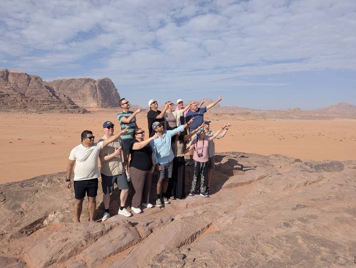 Group of travellers striking pointing poses atop a rocky ridge in the Wadi Rum desert.