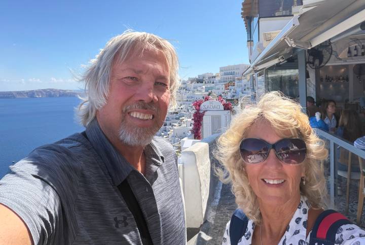 Couple selfie overlooking whitewashed buildings and deep blue caldera of Santorini.
