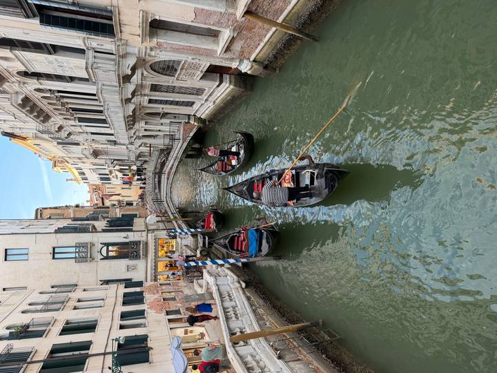 Gondoliers navigating narrow green canal flanked by historic Venetian buildings.