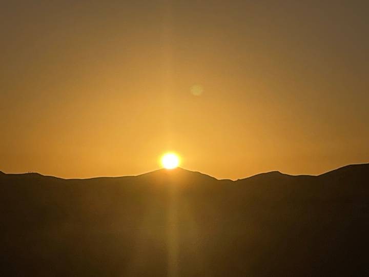 Golden sun setting behind low desert hills casting warm glow across the sky.