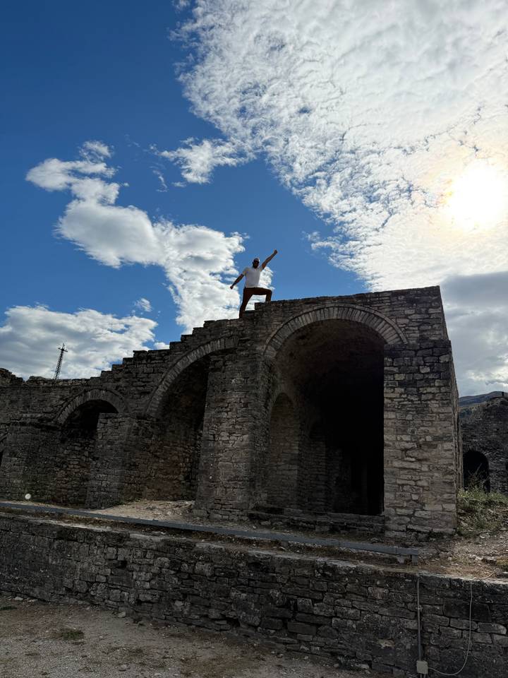 Silhouetted figure strikes a heroic pose atop ancient stone arches against a backdrop of bright clouds.