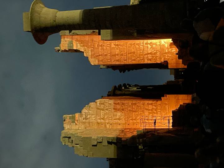 Dramatically lit entrance pylons of Karnak Temple glow amber against the night sky during a sound-and-light show.