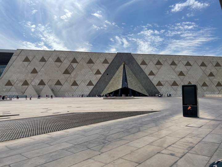 Modern triangular entrance of the Grand Egyptian Museum with expansive geometric façade under wispy clouds.