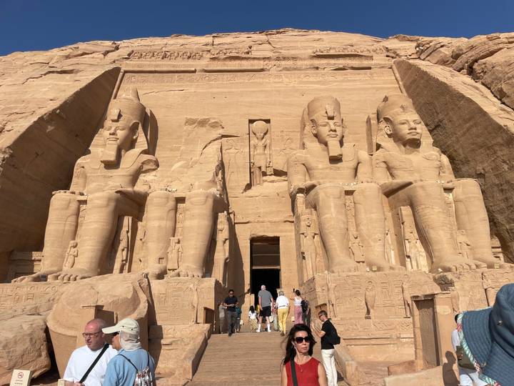 Colossal statues of Ramses II guard the entrance to Abu Simbel temple as early visitors gather below.
