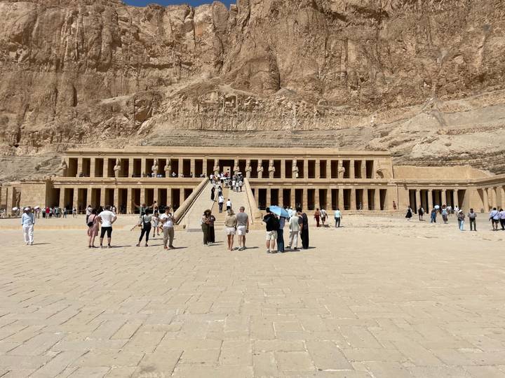 Visitors approach the terraced colonnades of Hatshepsut Temple set against towering desert cliffs.