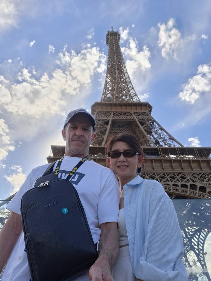 Couple selfie taken from below with the Eiffel Tower soaring into a partly cloudy sky.