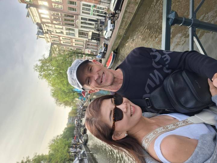 Couple posing on bridge overlooking an Amsterdam canal lined with historic houses and boats.
