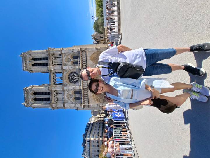 Couple posing in front of the façade of Notre Dame Cathedral on a bright blue day.