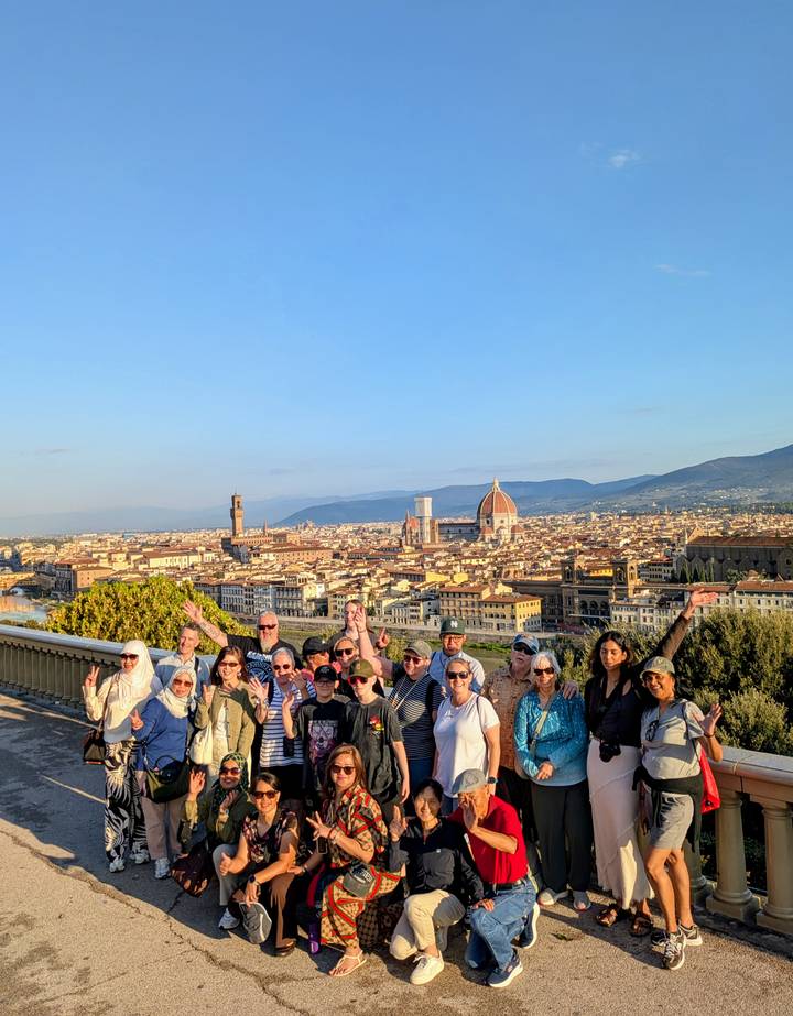 Large tour group posing with panoramic view of Florence skyline including the Duomo and Palazzo Vecchio at golden hour.