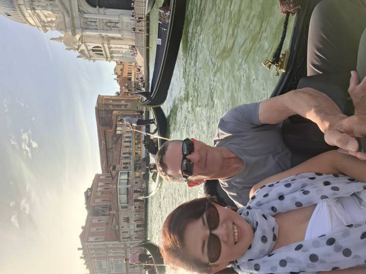 Couple riding in a gondola on Venice’s Grand Canal with other gondolas and historic buildings behind.