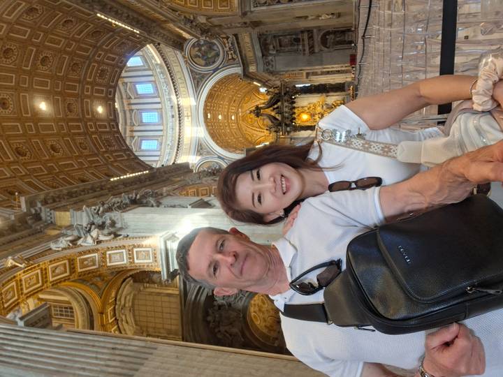 Couple inside the ornate interior of St. Peter’s Basilica with soaring dome and gilded decor.