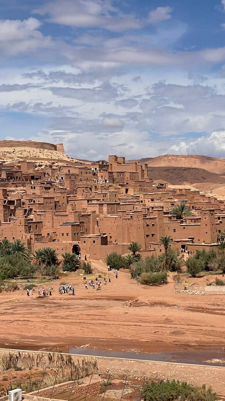The earthen kasbah of Ait Benhaddou rises in tiers against arid hills, palm trees dotting the foreground.