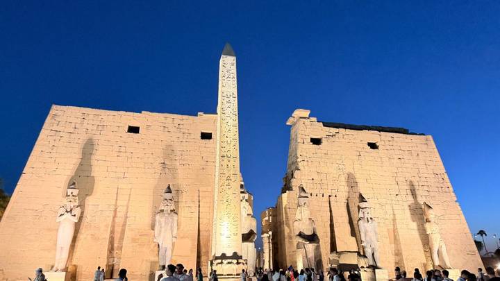 Luxor Temple illuminated against a deep blue evening sky with its towering obelisk.