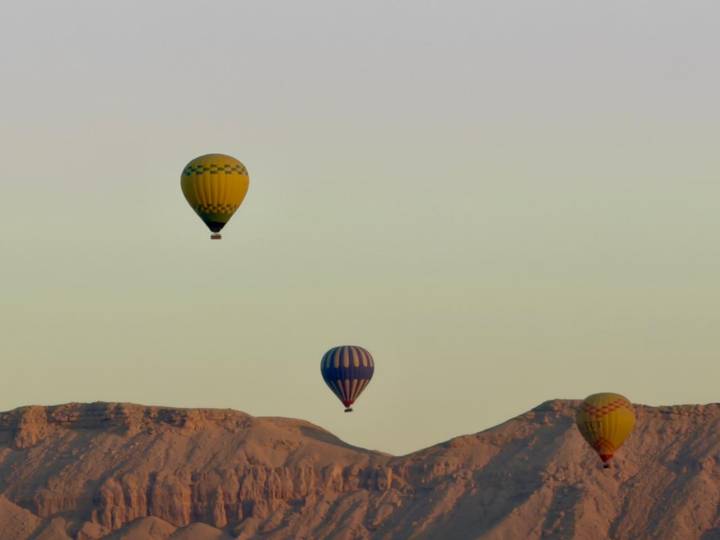 Colorful hot-air balloons float above desert mountains at dawn.