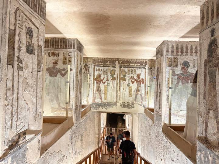 Visitors descend a richly painted corridor inside a pharaonic tomb.