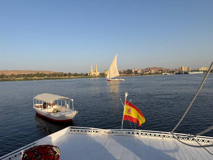 A felucca and motorboat sail on the Nile with Aswan’s riverside skyline beyond.