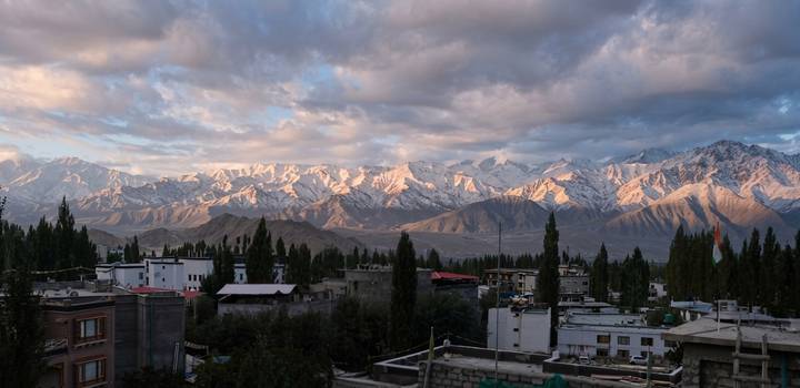 Sunset light bathes snow-dusted Himalayan peaks towering above Leh town’s rooftops and poplar trees.