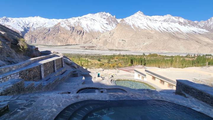 Tiered hillside resort pools and terraces face expansive stony plains and soaring snowy peaks.