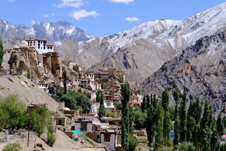 A cliff-side Himalayan village with whitewashed monasteries, green poplars and snow-dusted ridges in the background.