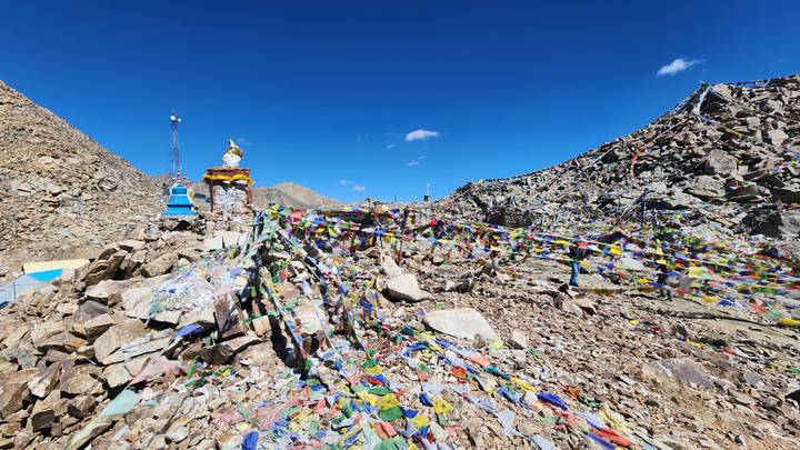 Rocky mountain pass strewn with colourful prayer flags beneath a vivid blue sky.