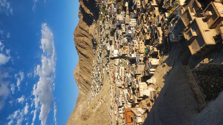 Panoramic view of Leh town sprawled across a valley, captured in warm late-afternoon light with rugged hills around.