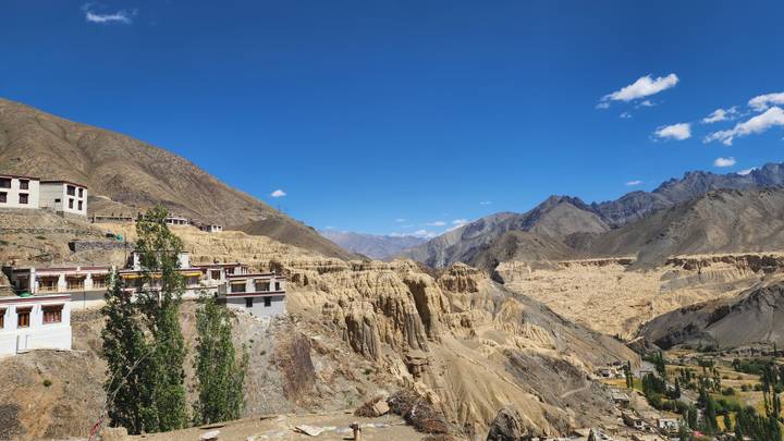A monastery sits on the edge of eroded beige cliffs overlooking a dramatic moonscape valley.