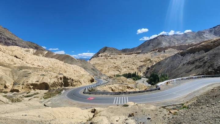 Wide view of a serpentine mountain road through eroded beige hills under a spotless blue sky.