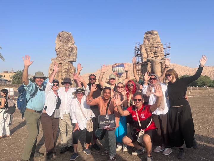 Tour group cheers with raised hands in front of the Colossi of Memnon with a balloon in the background.