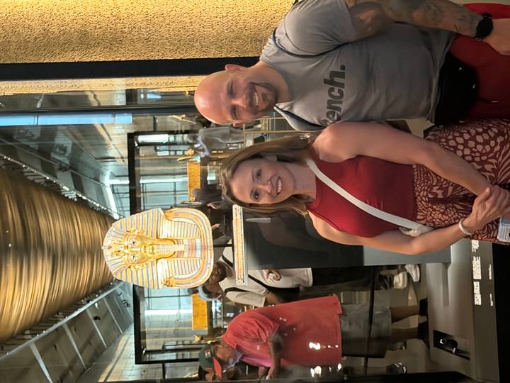 Visitors inside a museum standing in front of Tutankhamun’s golden mask display.