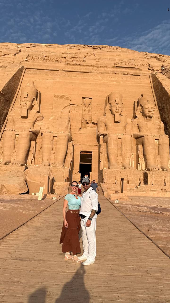Couple standing before the colossal statues of Abu Simbel temple bathed in warm sunlight.