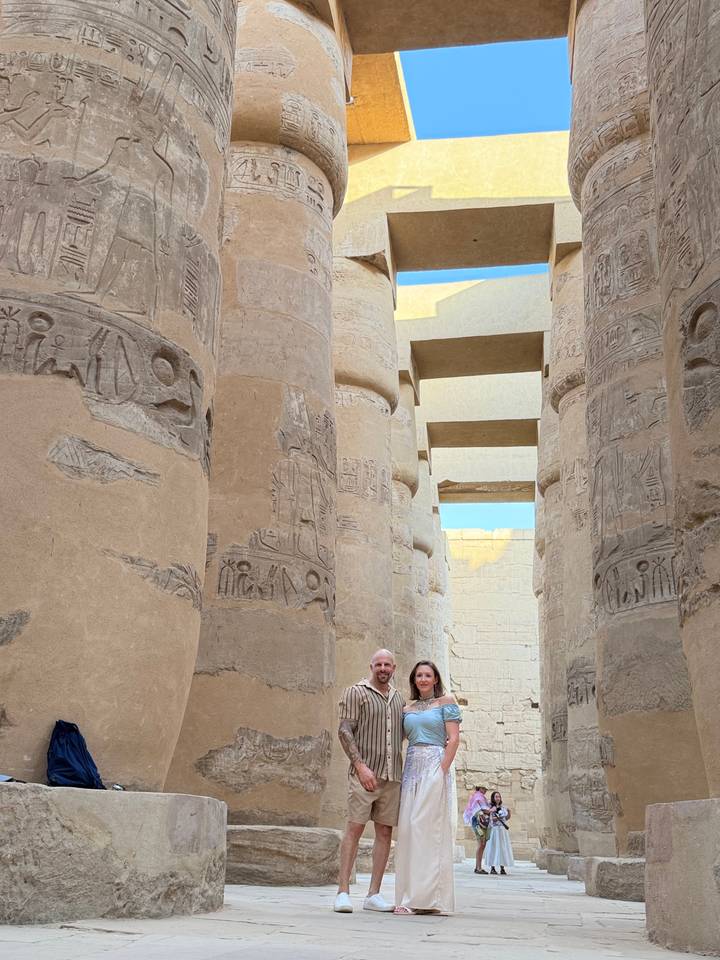 Travelers between towering carved columns covered in hieroglyphs at Karnak Temple complex.