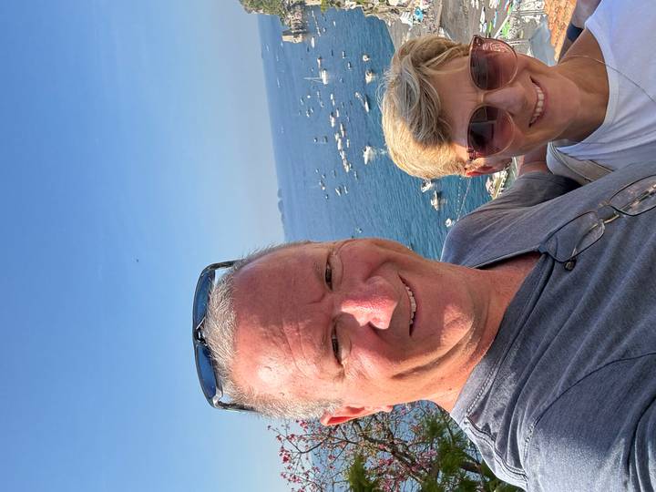 Selfie of a couple overlooking a sparkling Mediterranean bay dotted with boats on a clear day.