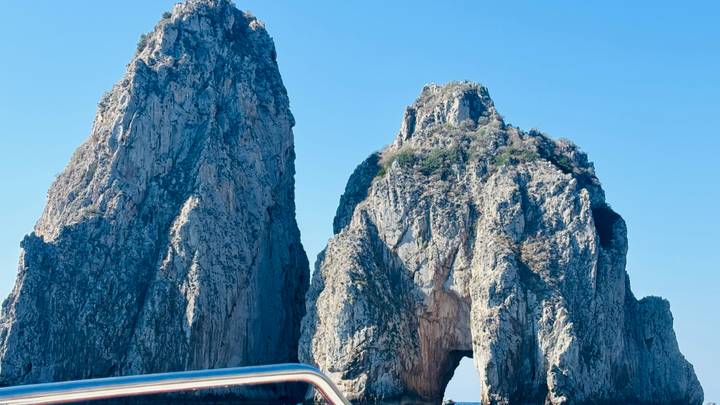 Towering limestone stacks of the Faraglioni rise out of Capri’s blue waters, viewed from a boat.