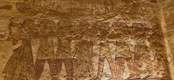Warmly lit close-up of ancient Egyptian relief carvings depicting a ceremonial procession on a stone wall.