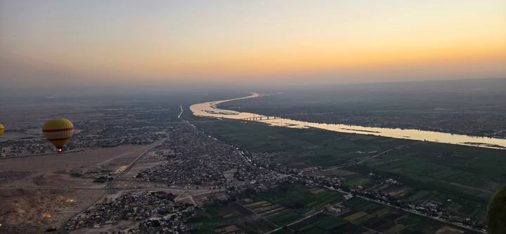 Aerial dawn view of the Nile River winding through farmland with a single hot-air balloon drifting to the side.