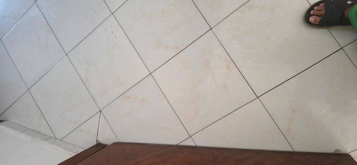 Plain indoor ceramic tile floor with a small portion of a sandal-clad foot in the corner.